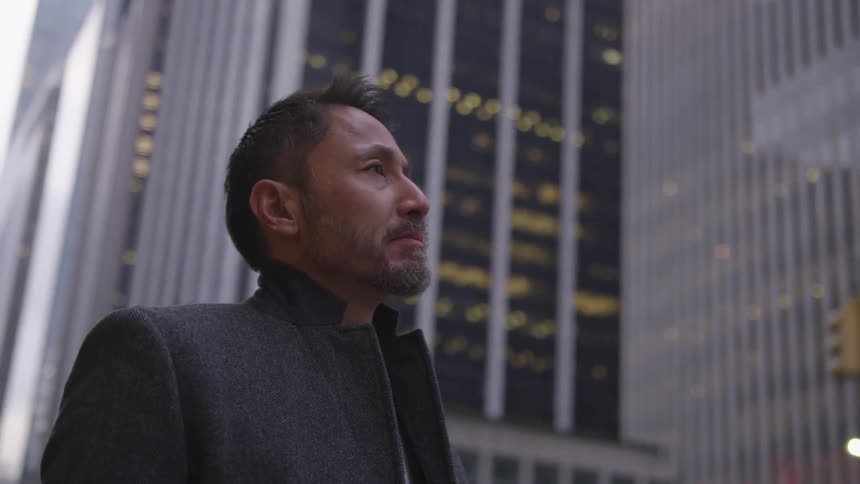 A man stands on a city sidewalk near skyscrapers