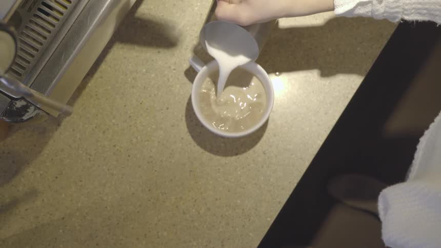 A person pours milk in their mug