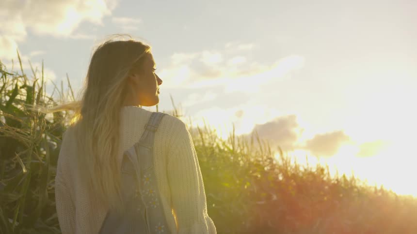A woman walks by a corn field at sunset
