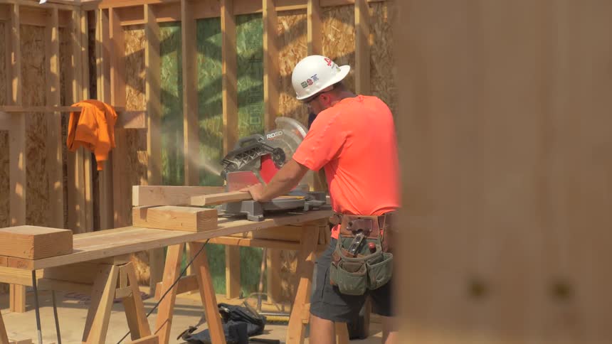 A man uses a saw to cut lumber on a sunny day
