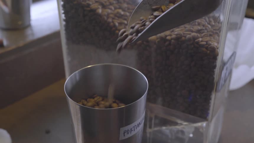 Coffee beans are being scooped from a container into a measuring cup in daylight