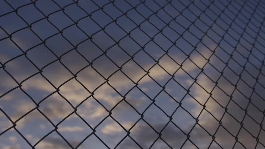 Clouds float in the sky behind a chain link fence