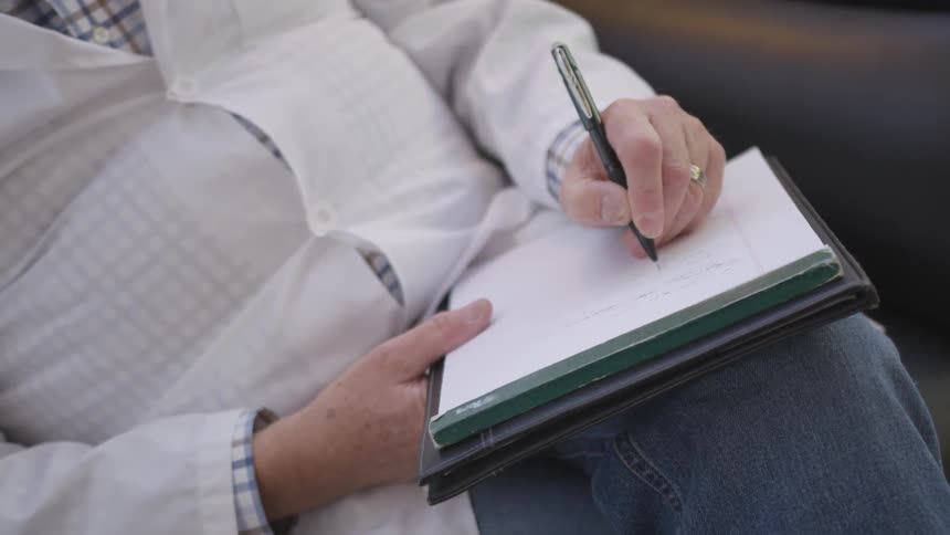 Person sits in a chair writing on a notepad