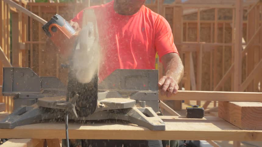 Sawdust flies as a man trims lumber