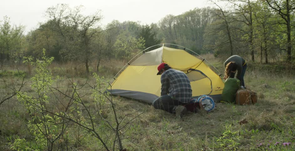A man and woman set up a tent in the woods