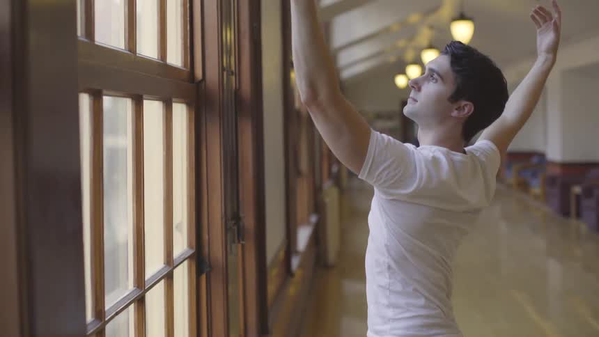 Man does ballet moves while standing in front of a window