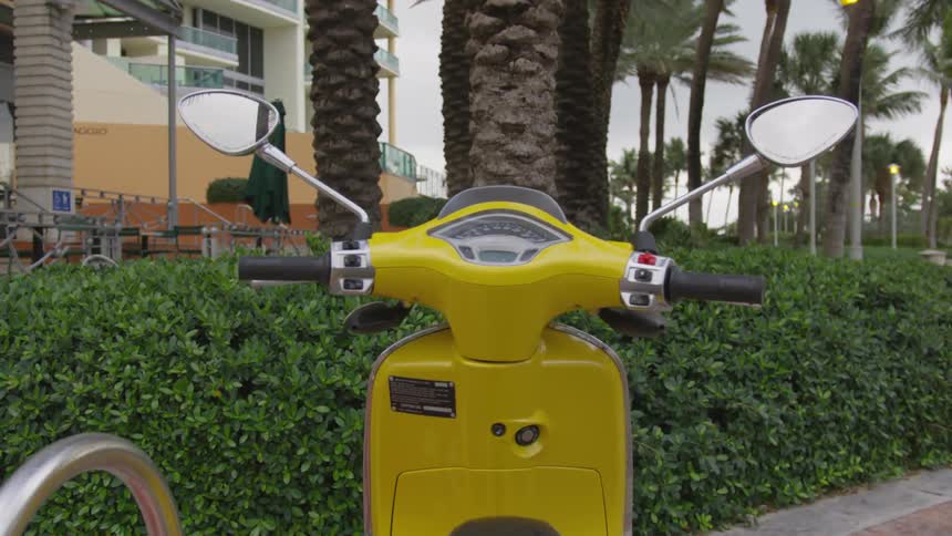A yellow motor scooter parked outside a building with palm trees