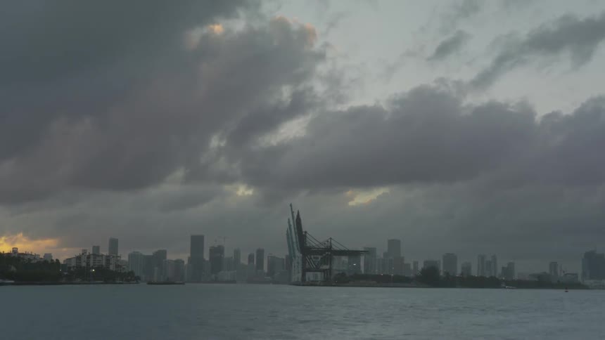 Boats are traveling through a city harbor as dusk falls