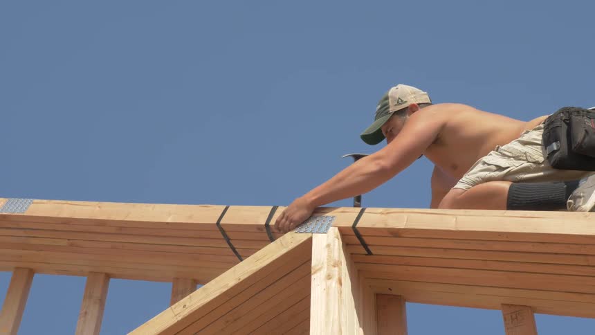 Man hammers wooden beams while kneeling on them