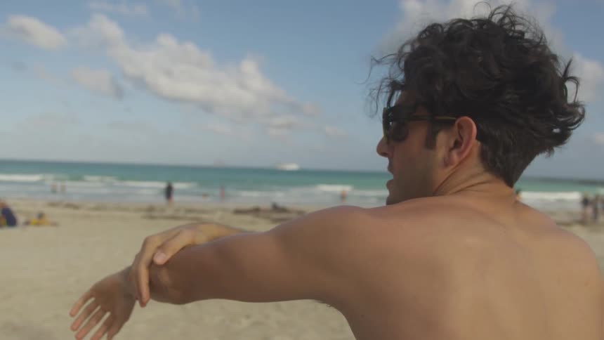 A man rubs his arm while sitting on a beach