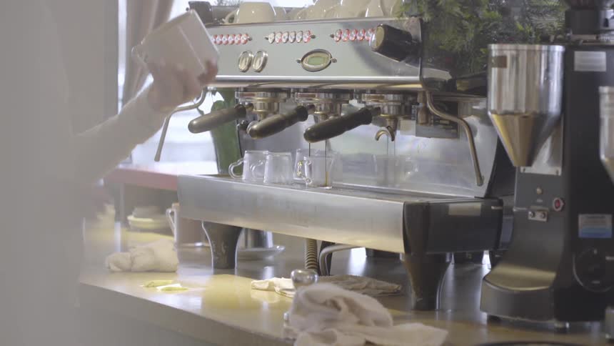 A woman takes a coffee cup off of the top of an espresso machine