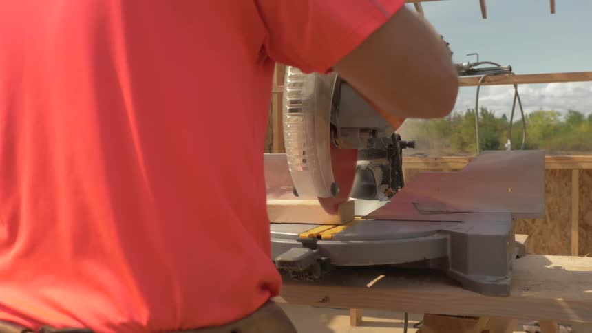 A man uses a saw to trim a piece of lumber