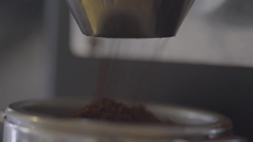Ground coffee is pouring from a machine into a container