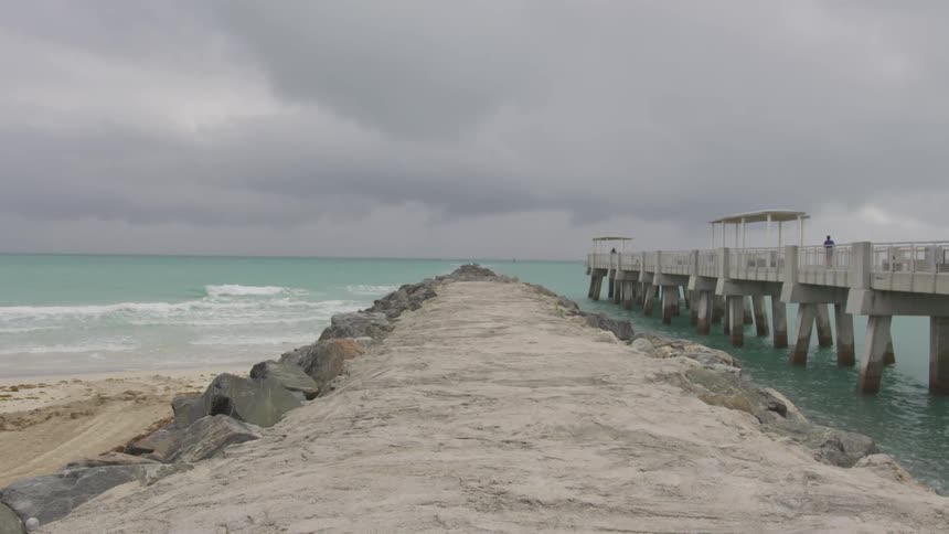 A person is walking on a pier at a beach on a stormy day