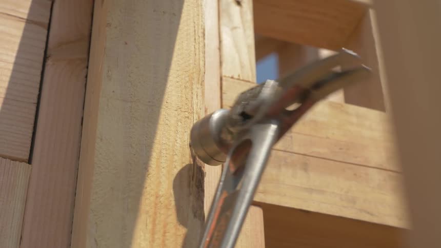 A construction worker is hammering a nail outside in daylight