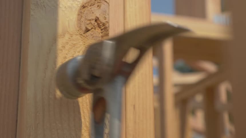 A builder hammers a nail into wood framing
