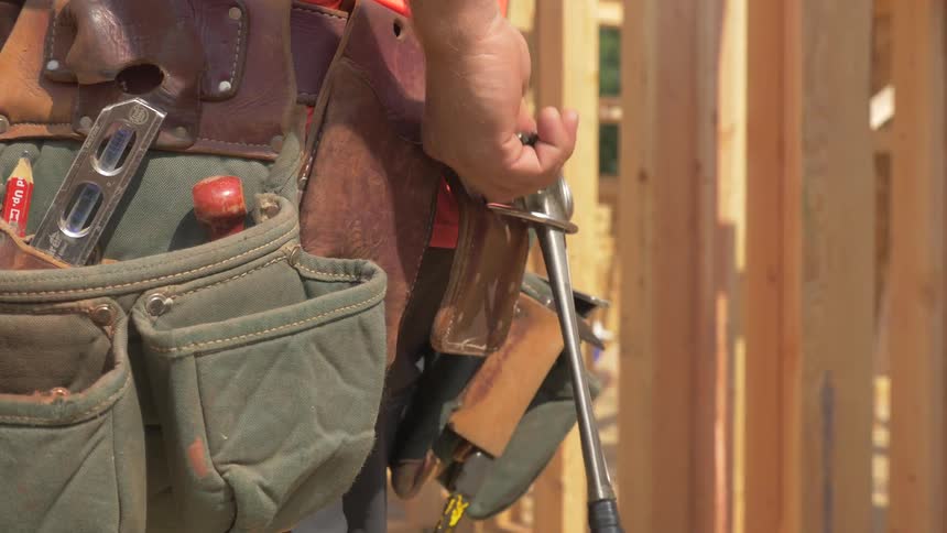 A man reaches and pulls the hammer out of his tool belt