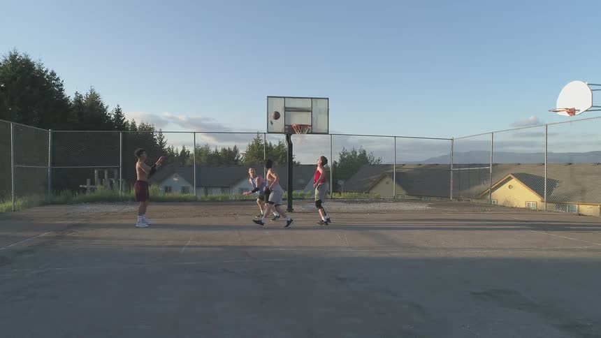 Several boys play basketball in an outside court