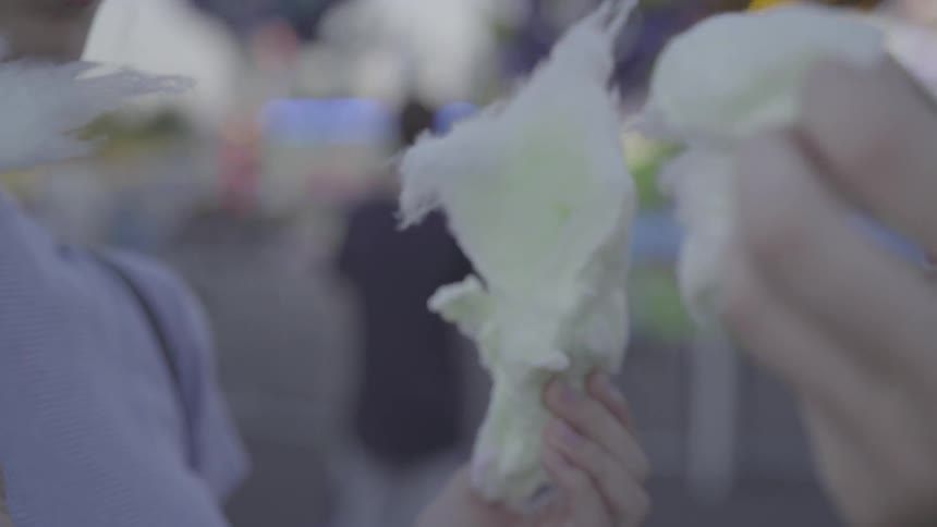 A couple are tearing bites from a piece of cotton candy outside in daylight