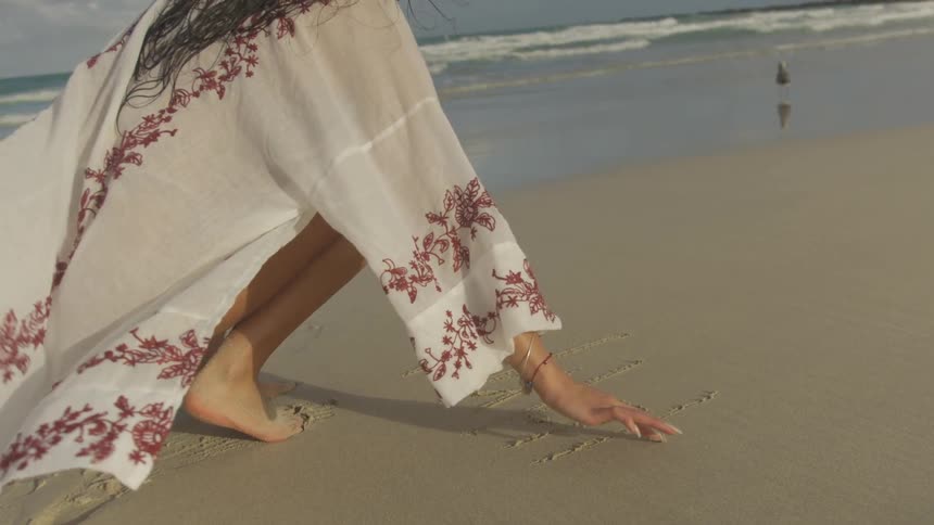 A woman draws in the wet sand