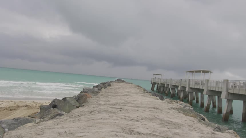 Storm clouds are hanging over a pier at a beach in daylight