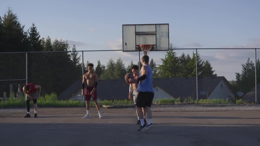 Several teenagers play basketball on an outside court