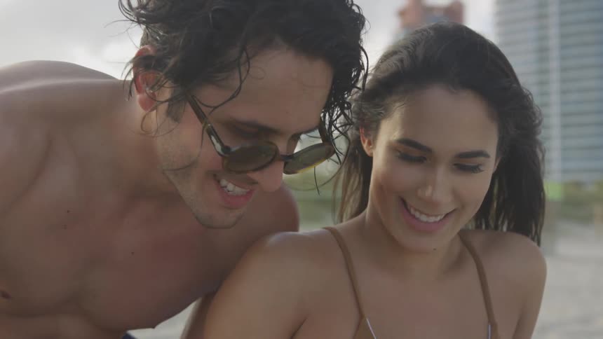 A man leans over a woman's shoulder on the beach