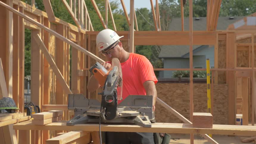 The construction worker is using a table saw to cut wood