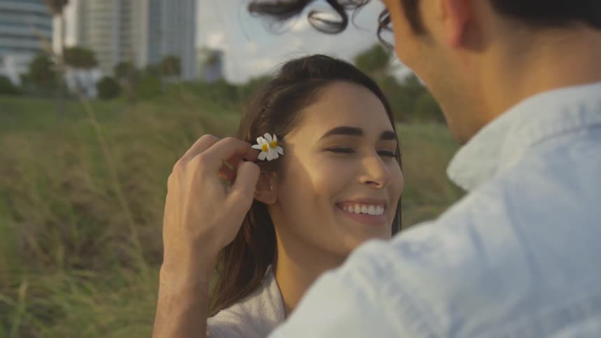 The woman smiles as he puts a flower in her hair