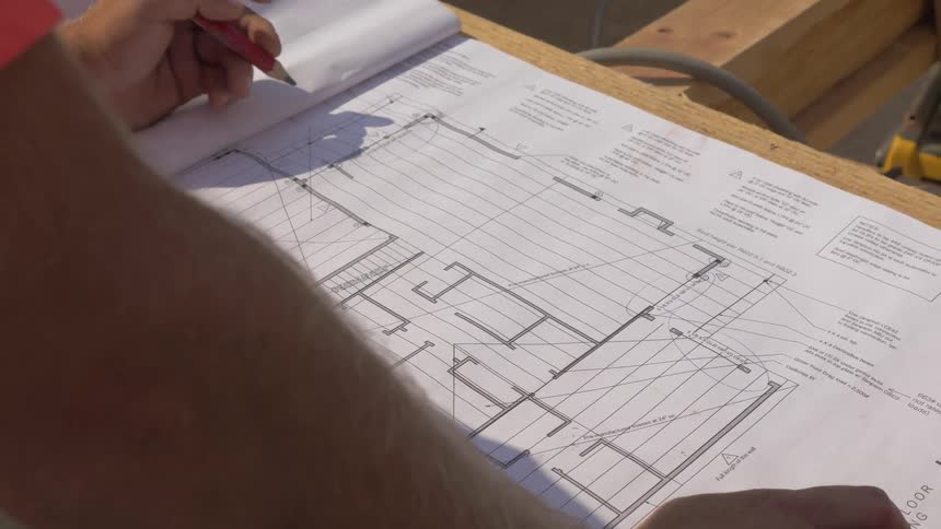 A man is taking notes on a blueprint outside in daylight