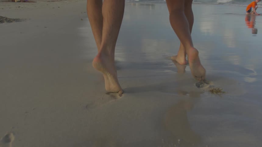 Two people walk barefoot on the sandy shore
