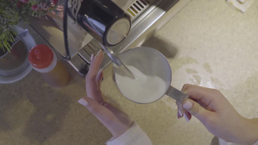 A barista in a coffee shop is making steamed milk for a coffee