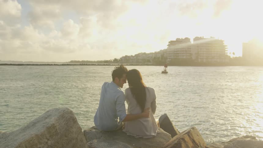 A couple sit on the rocks together by the water