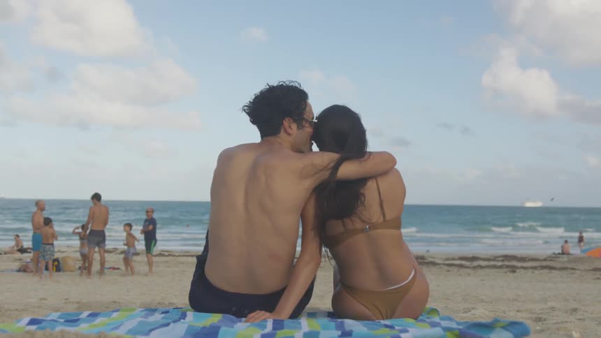 A man and woman hug as they sit on the beach