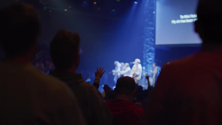 Band plays on stage while many people in the Audience sway and raise their arms