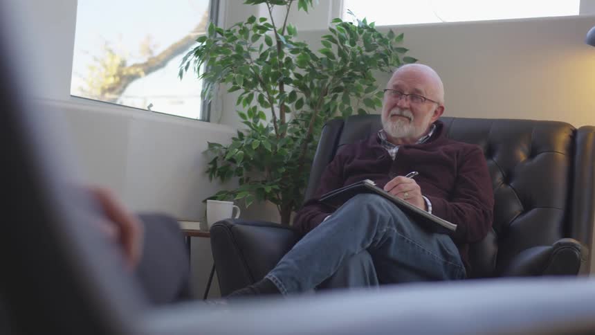 Therapist is sitting in chair and talking to another person