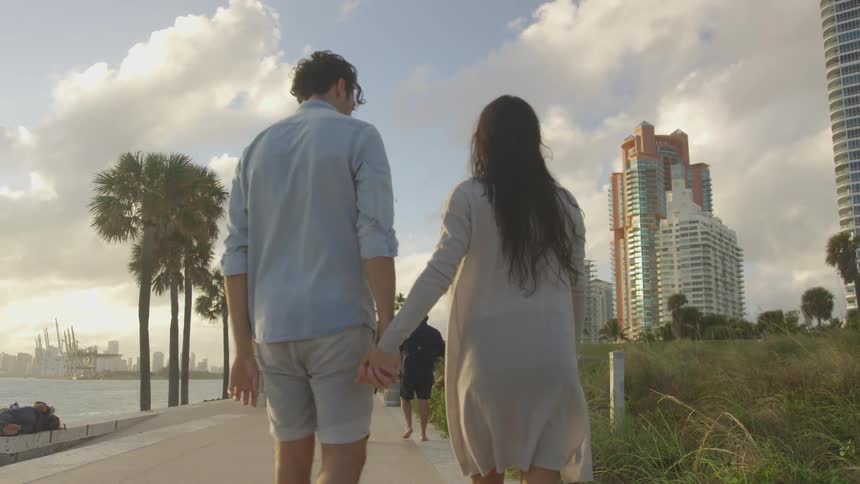 A couple holds hands as they walk on a path by the water