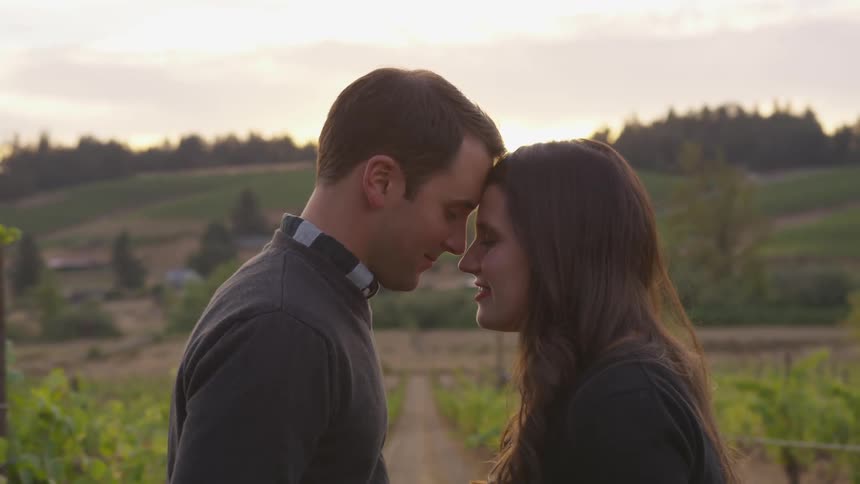 A man and woman stand head to head in a vineyard