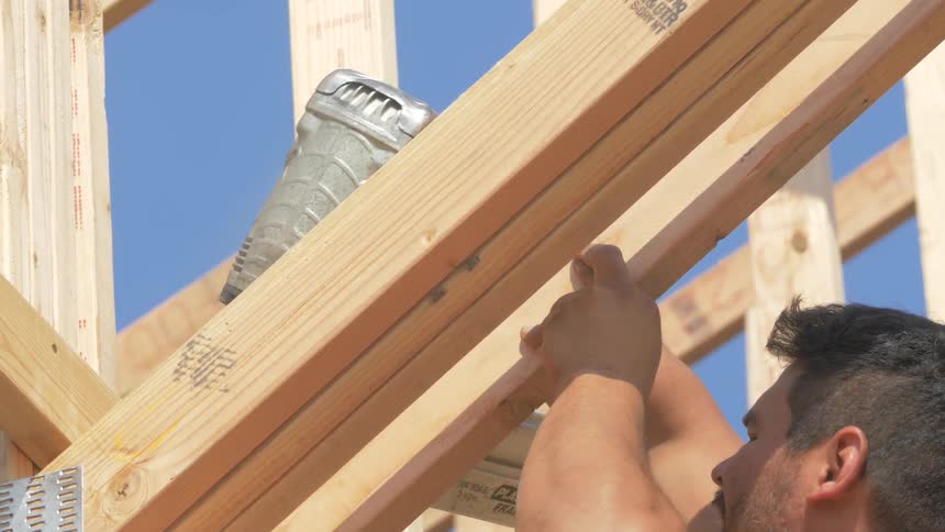 A man nails some beams on a house