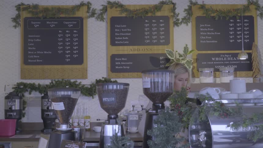 A barista is working behind a counter in a coffee shop in daylight