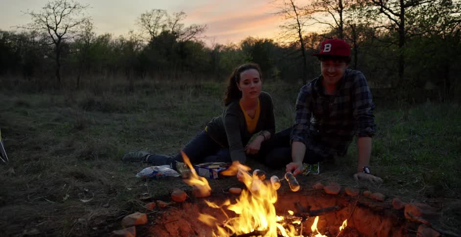 Young couple roasting marshmallows at a campsite at sunset