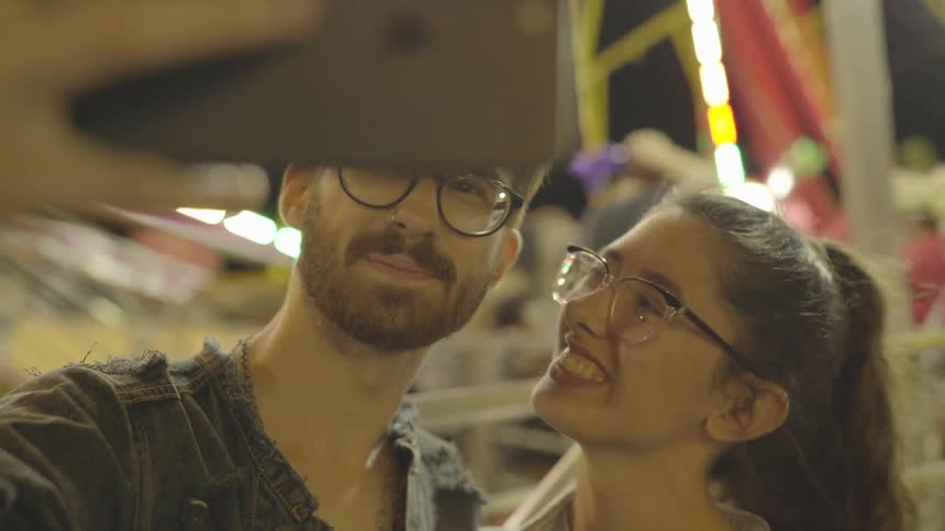 A couple are taking a selfie at a fair at night