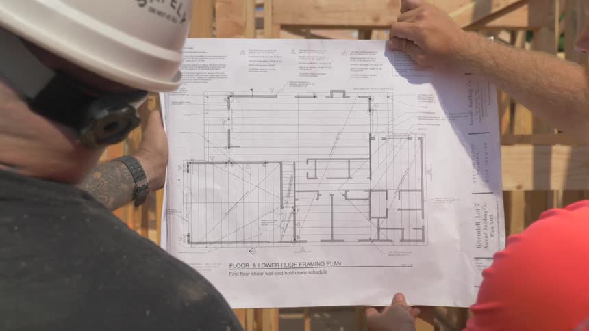 Construction workers are reviewing blueprints outside in daylight
