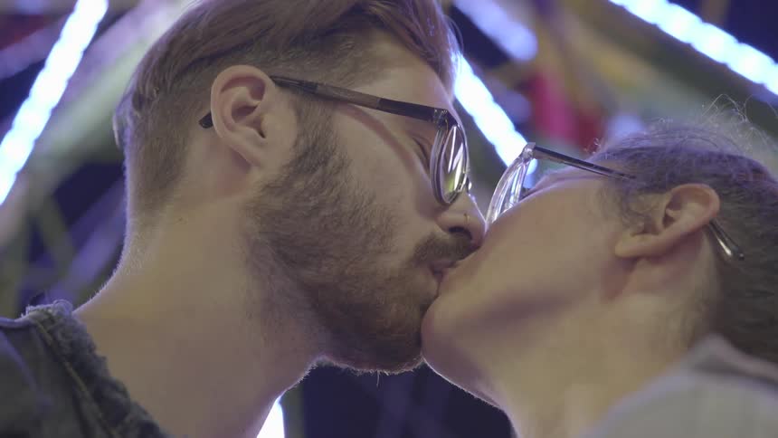 Man and woman kiss at a fair at night