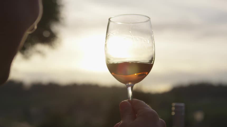 A man swirls wine in a glass at sunset