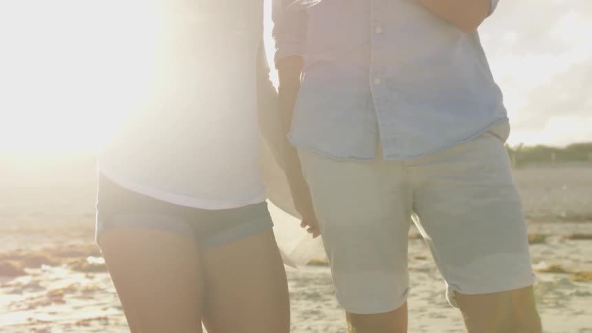 A couple holds hands and wine glasses as they walk on the beach