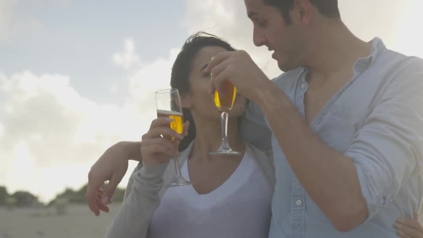 A couple are clinking their champagne glasses together as they stand outside in daylight
