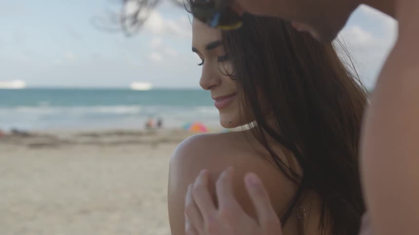 A man smooths sunscreen on a woman's shoulder and back at the beach