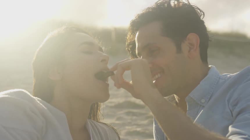 Man feeds woman a piece of food while laying on the beach