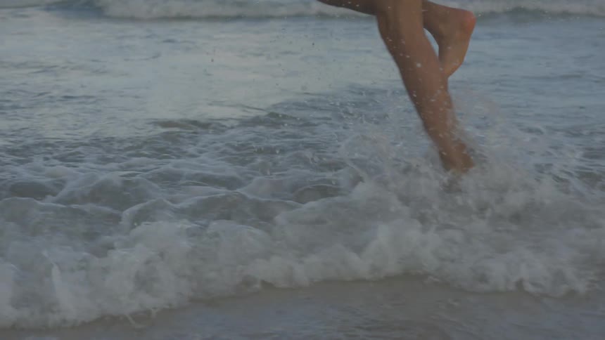 Person runs on the beach splashing in shallow water